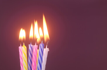 Several different birthday cake candles burning on purple background. Copy space for text.