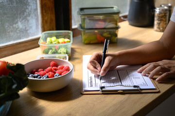 Nutritionist writing a healthy meal plan with fresh fruits, vegetables, and nuts on the table