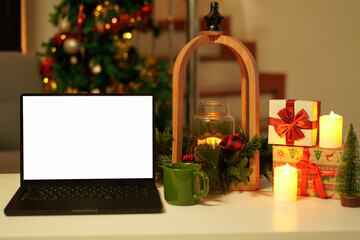 Blank display screen laptop computer on white wood table. Modern cozy comfortable home living room with Christmas decor. Home office desk workspace.