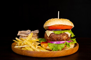 Delicious hamburger with cola and potato fries on a wooden table with a dark brown background behind. Fast food concept.