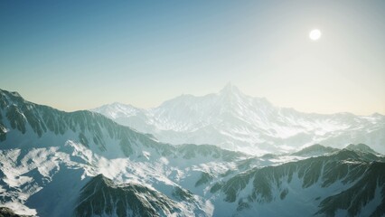 Towering peaks stretch toward the sky, their snowy caps glimmering under the bright sun. A soft haze envelops the vast terrain, creating a serene ambiance in this breathtaking mountain landscape.