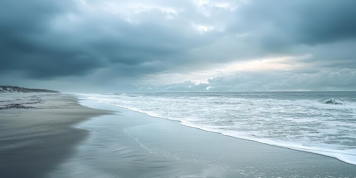 A vast, expansive ocean with waves crashing onto the shore, under a cloudy sky with dark clouds and a hint of sunlight breaking through, casting a dramatic light on the water and the beach.