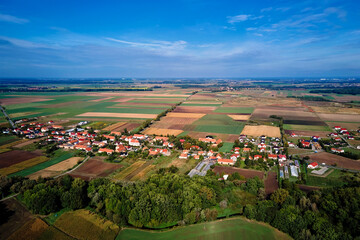 Aerial view of small village with red roofs surrounded by agricultural fields and forest