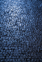 Blue cobblestones on a street sidewalk in Porto (Portugal). Shiny historic basalt ashlars and blocks reflecting the sky. Pavement background, dark blue reflections at dusk or dawn twilight.