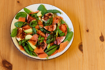 Healthy salad with smoked salmon, spinach, avocado and fig on wooden table