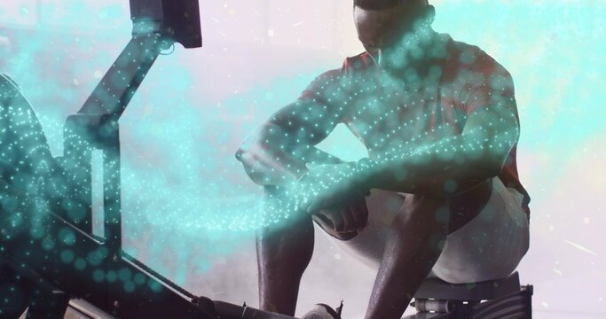 Rowing fit man gripping handlebar on rower in fitness studio, with digital particle overlay