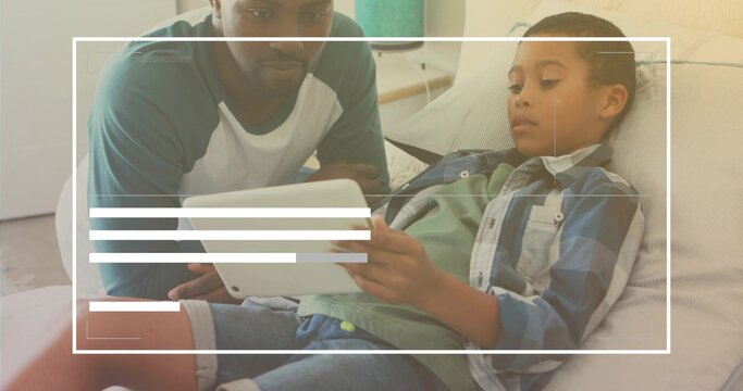 Watching African American man and child using tablet on living room couch with cushions, side table