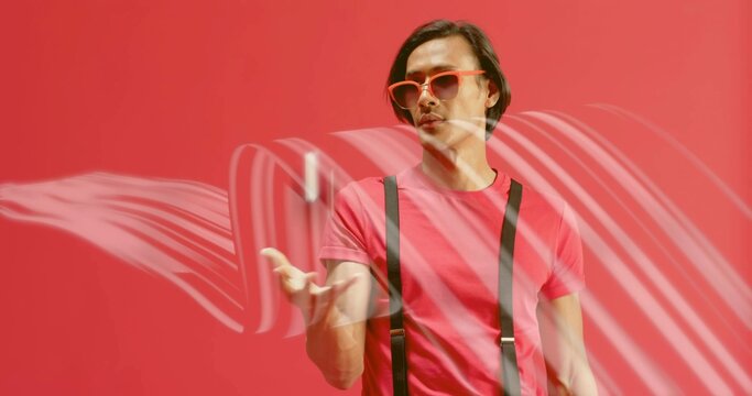 Tossing smartphone, Asian man wearing red tee and red sunglasses creating motion blur in studio