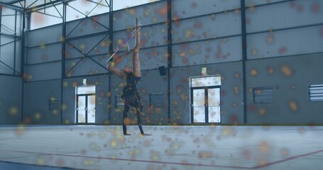 Rhythmic gymnast in leotard doing one-handed handstand on white floor in gym, with hoop, red lines