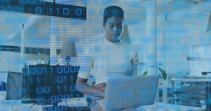 Working woman wearing white t-shirt typing on laptop in open-plan office, with monitor and plant