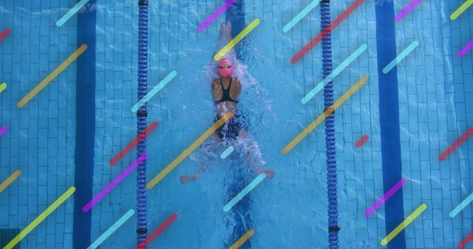 Slicing female swimmer cutting through pool lanes at aquatic center, with pink swim cap and goggles