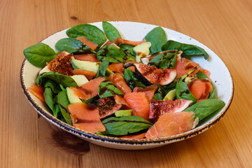 Healthy salad with smoked salmon, spinach, avocado and fig on wooden table