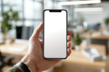 Close-up of hand holding a modern smartphone with empty white display, set against blurred background of contemporary office space.