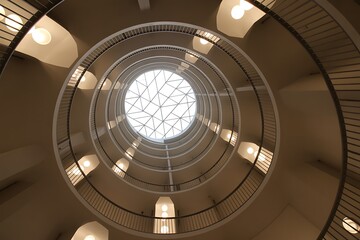 Dramatic upward view of stunning architectural spiral staircase with geometric skylight evokes a sense of ascension and modern design in a unique building