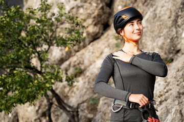 Young Caucasian female athlete in climbing gear warming up before training session on natural rock, focus on sports preparation, stretching and body readiness for performance