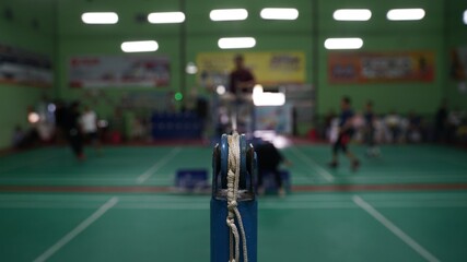 Badminton net straps attached to poles with badminton court in blur background