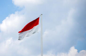 Waving the red and white Indonesian flag ('Merah Putih') against a bright blue sky with clouds. A symbol of national pride, patriotism, and freedom