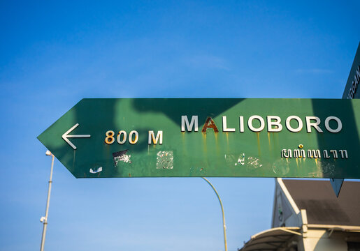 The iconic Malioboro Street sign in Yogyakarta, Indonesia. This vintage-style green signpost, featuring Javanese script, points travelers toward the famous cultural and shopping destination.