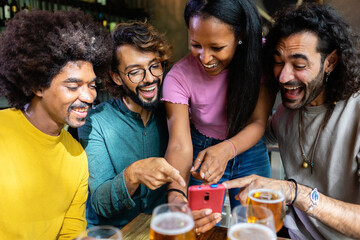 Cheerful multi-ethnic friends having fun together, drinking beer and using a smartphone at the bar
