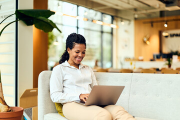 African-American Woman Working on Laptop in Modern Office Lounge, Smiling and Focused