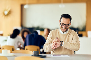 Casual Businessman Glances at Watch During Team Meeting in a Modern Café