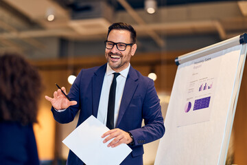 Confident Business Presenter In Navy Suit Demonstrates Monthly Sales Report To Colleague At...