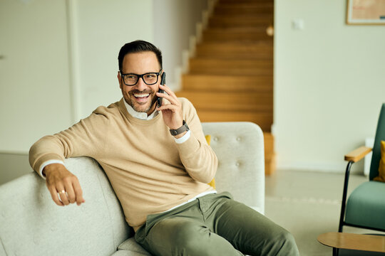 Casual Businessman Smiling While Talking on Phone at Home, Relaxed on Sofa in Modern Living Room - Powered by Adobe