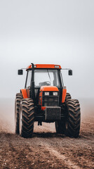 Obraz premium Red farm tractor on muddy field with foggy sky