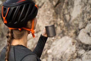 Back view of young woman rock climber taking break and drinking from titanium mug with rock wall background, outdoor recreation, travel hydration and sustainable adventure lifestyle concept
