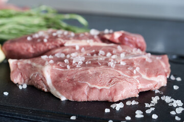 Raw fresh beef steak with salt and herbs on a black cutting board