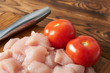 Raw chicken fillet and tomatoes on a cutting board, closeup