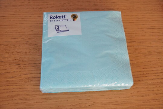 A neatly stacked pack of light blue Kokett serviettes, labeled '20 SERVIETTEN', in its original plastic packaging, displayed on a wooden surface