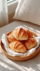 Golden baked croissants served on a white cloth inside a wooden plate with natural light casting shadows on a bright morning