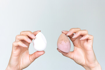 A woman's hands holding a dirty and clear makeup sponges against a gray background. Timely hygiene...