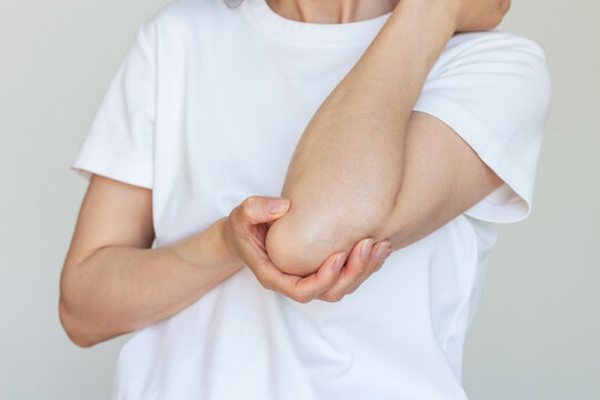Young caucasian woman in white tshirt holding the elbow joint, experiencing pain from arthritis, elbow injury.