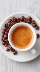 Overhead View Of A White Ceramic Cup Filled With Rich Espresso Coffee Surrounded By Dark Roasted Coffee Beans On A White Saucer Placed On A Textured White Wooden Surface