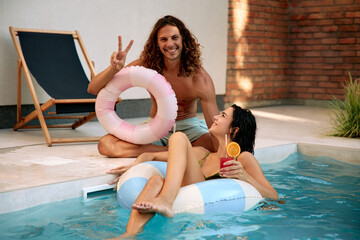 Man and woman enjoying poolside time with inflatable and drink