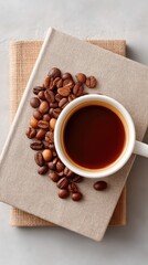 Overhead View Of A White Coffee Cup Filled With Dark Coffee Next To A Pile Of Roasted Coffee Beans On A Textured Surface With A Neutral Background