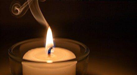 Burning candle in a glass holder with smoke against a dark background.