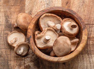 Raw shiitake mushrooms in wooden bowl on the table, top view.