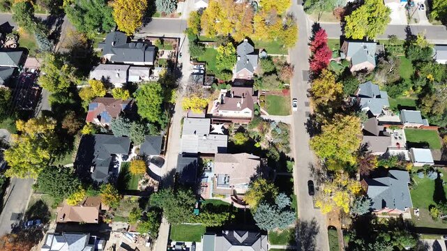 Home under roof construction wrapped in envelope cover in suburbs Denver, CO neighborhood surrounded by solar panel rooftops and mature trees in peak fall color. Quiet and clean street layout