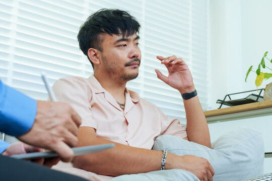 Asian adult man sitting in therapy session with senior therapist, expressing emotion while reflecting on personal issue listening advice, representing process self awareness emotional healing