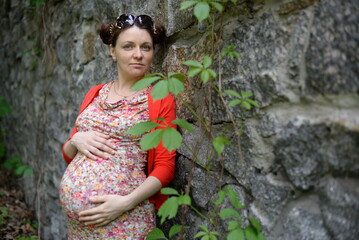 Beautiful pregnant girl in a red blouse against a stone wall background