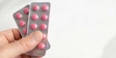 Person holding pink pills in blister packs on blurred background