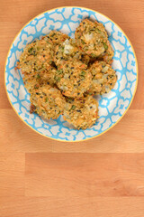 A small stack of golden-brown vegan soy patties is served in a decorative white and blue patterned bowl on a wooden tabletop with copy space below