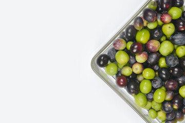 An overhead shot of a glass dish filled with mixed green and black olives, positioned in the bottom right corner on a clean white background with copy space
