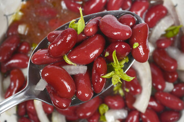 A close-up shot captures a spoonful of glossy, dark red kidney beans, white onion, and herbs lifted...