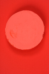 A round piece of red or coral modeling clay is placed on a matching solid red-orange background, creating a monochromatic composition