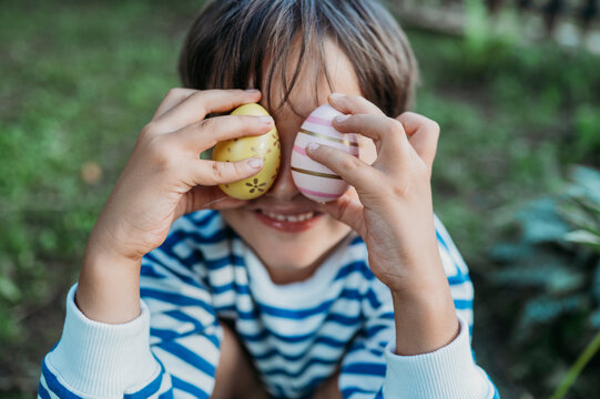 Smiling boy covering eyes with multi colored easter eggs in park