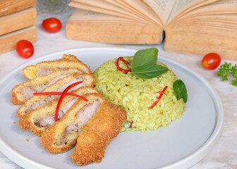Crispy fried chicken cutlets served with vibrant green rice. The dish is garnished with red pepper and green basil leaves